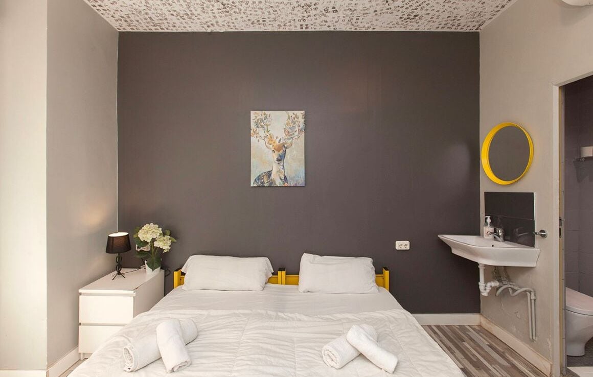 Een moderne hotelkamer met een bed, nachtkastje, schilderij, spiegel en een badkamer.