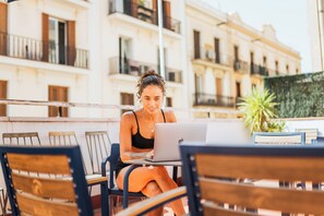 A person seated at a table with a laptop, in an outdoor setting with a building in the background. - Hey Lola Hostel (Barcelona)