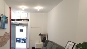 A modern hotel lobby with a grey sofa, a reception desk, a framed welcome sign, and a potted plant. - Hey Lola Hostel (Barcelona)