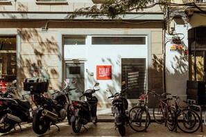 A row of parked motorcycles and bicycles outside a building with a large door and a sign that reads 'LOCALE EN ALQUILER'. - Hey Lola Hostel (Barcelona)