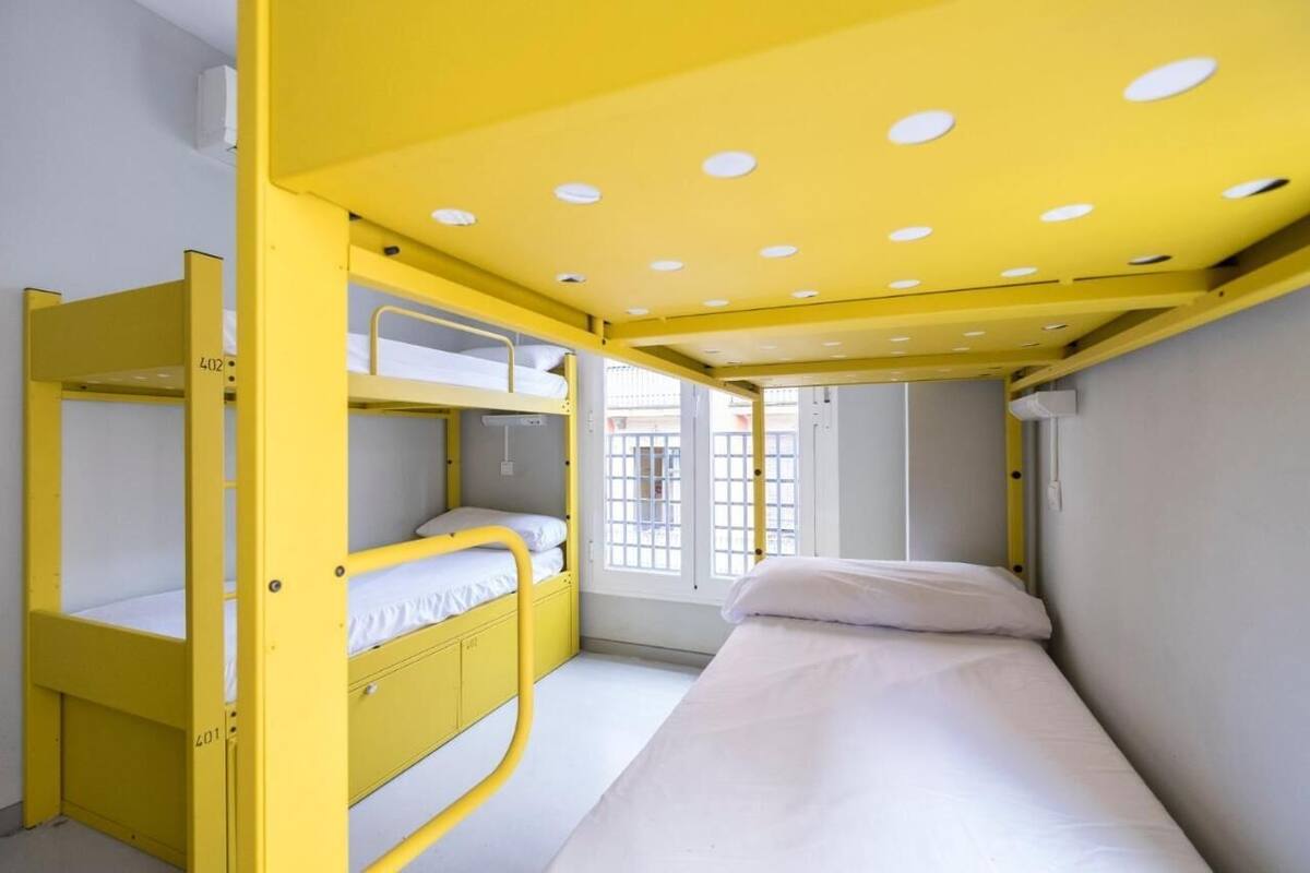 Een kleine, helder verlichte kamer met gele stapelbedden en een enkel bed.