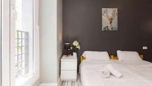 A bedroom with a bed, a nightstand, a lamp, and a painting on the wall. - Hey Lola Hostel (Barcelona)