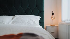 A neatly made bed with white linens, a dark green tufted headboard, and a bedside table with a lamp.