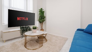 A modern living room with a flat-screen TV, a round table, a blue sofa, and a potted plant.
