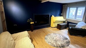 Ein Wohnzimmer mit dunkelblauer Wand, Kamin, gelbem Sideboard, grauem Sofa und rundem Teppich.