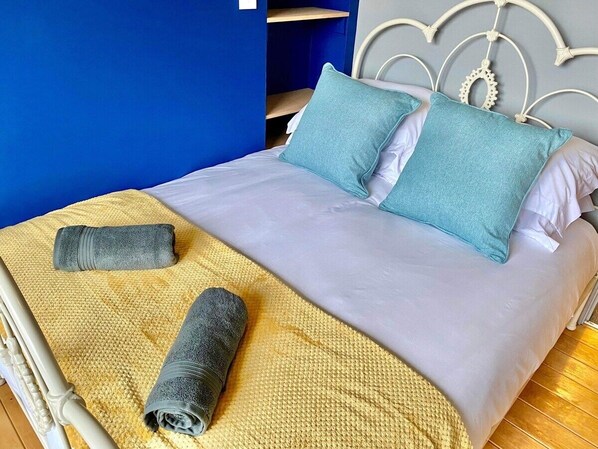 A bed with a white mattress, two teal pillows, and a yellow knitted blanket.