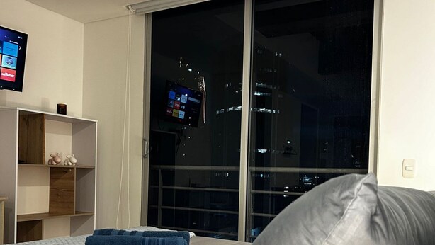 A bedroom with a bed, a large window, and a TV on the wall. - Hermoso apartamento con vistas 312 (Bogotá)