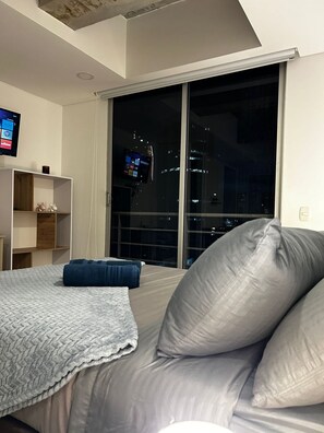 A bedroom with a bed, a large window, and a TV on the wall. - Hermoso apartamento con vistas 312 (Bogotá)