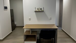 A modern, minimalist room with a wooden desk and chair, a small shelf with decorative items, and a recessed ceiling light. - Hermoso apartamento con vistas 312 (Bogotá)