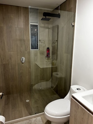 A modern bathroom with a glass-enclosed shower, a white toilet, and a wooden vanity. - Hermoso apartamento con vistas 312 (Bogotá)