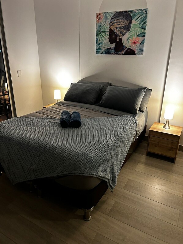 A bedroom with a bed, two bedside lamps, a nightstand, and a wall-mounted painting. - Hermoso apartamento con vistas 312 (Bogotá)