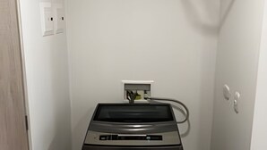 A compact laundry room with a front-loading washing machine, a drying rack, and a power outlet on the wall. - Hermoso apartamento con vistas 312 (Bogotá)