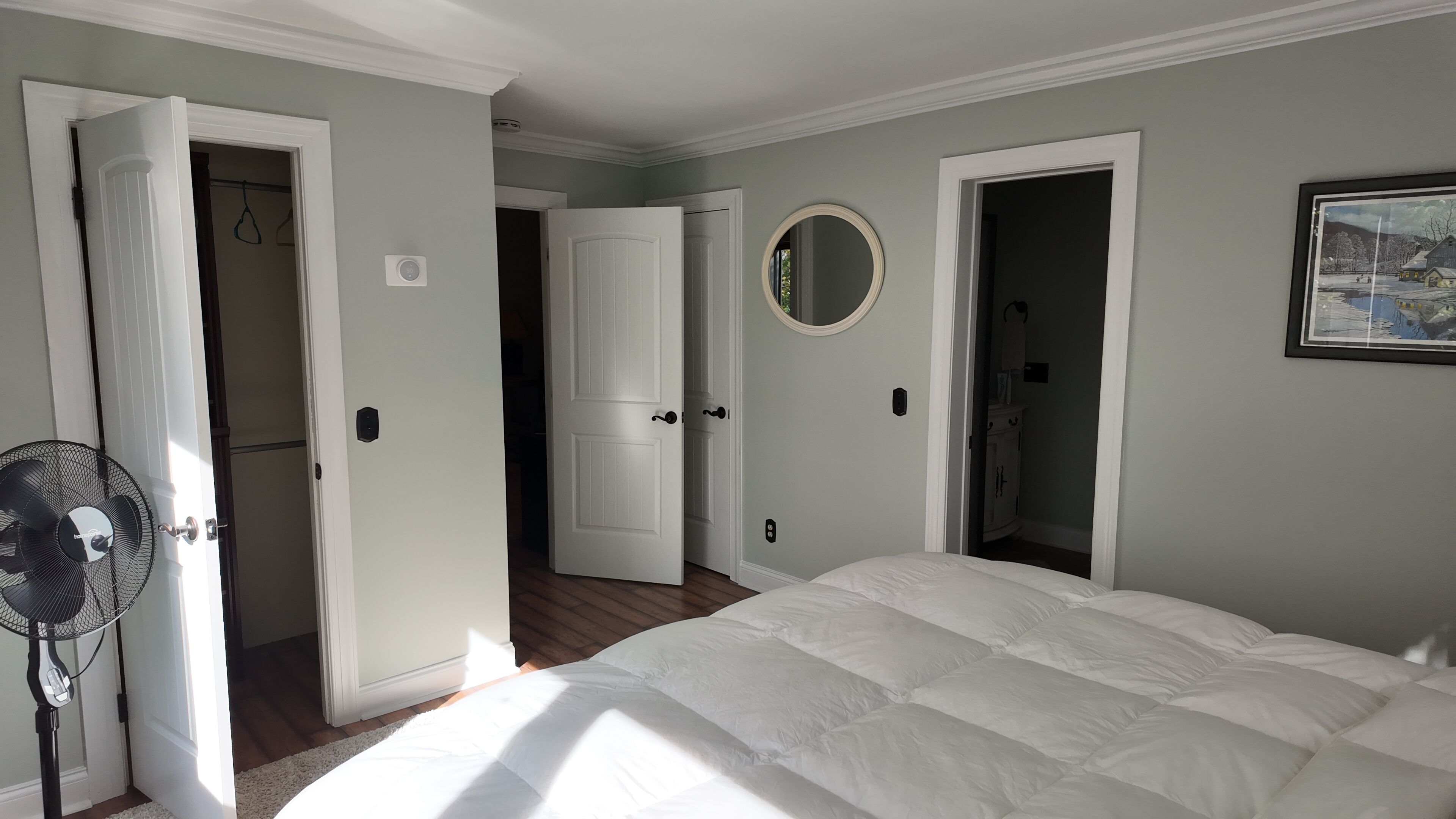 A bedroom with a bed, a standing fan, and two open doors leading to other rooms.