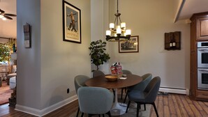 A dining area with a round table, chairs, a chandelier, framed pictures, and a potted plant.