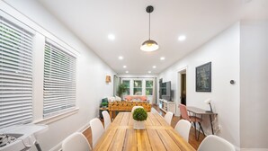 Un comedor con una mesa de madera, sillas blancas, una planta pequeña en maceta y un sofá con cojines.