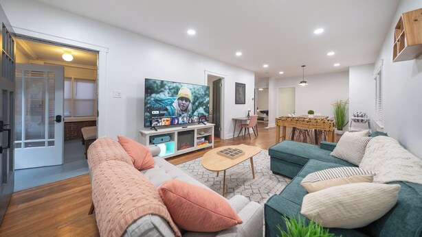 Una sala de estar moderna con un televisor de pantalla plana grande, un sofá, una mesa de centro y un comedor con una mesa y sillas.