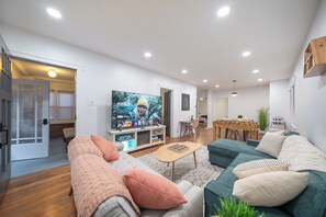 Una sala de estar moderna con un televisor de pantalla plana grande, un sofá, una mesa de centro y un comedor con una mesa y sillas.