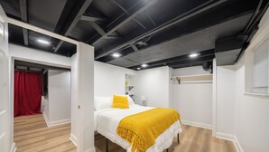 Un dormitorio con cama, paredes blancas, suelo de madera y techo con vigas a la vista.