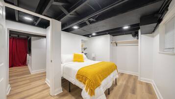 A bedroom with a bed, white walls, wooden flooring, and a ceiling with exposed beams.