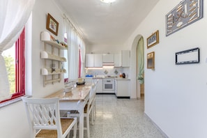 A compact kitchen with white cabinetry, a dining table with chairs, and a window with red curtains.