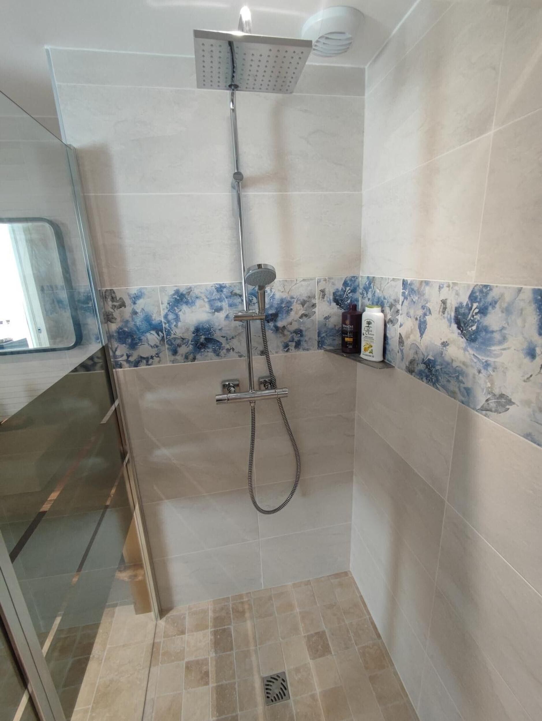 Une douche équipée d’un pommeau de douche à main, d’un robinet mural et d’un panneau de commande.