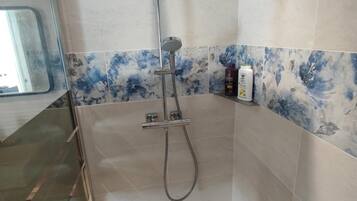 Une douche équipée d’un pommeau de douche à main, d’un robinet mural et d’un panneau de commande.