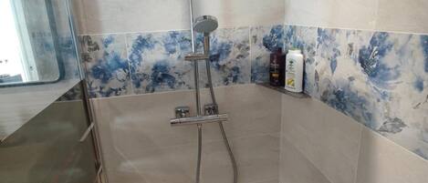 Una ducha con cabezal de ducha de mano, grifo de pared y panel de control.