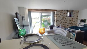 A dining area with a table set for two, a view of the outdoor patio, and a room with a stone wall and a bed.