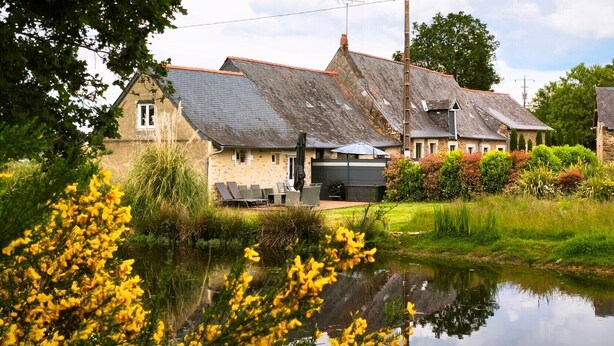 A house with a pond in front, a patio with chairs, and a garage.