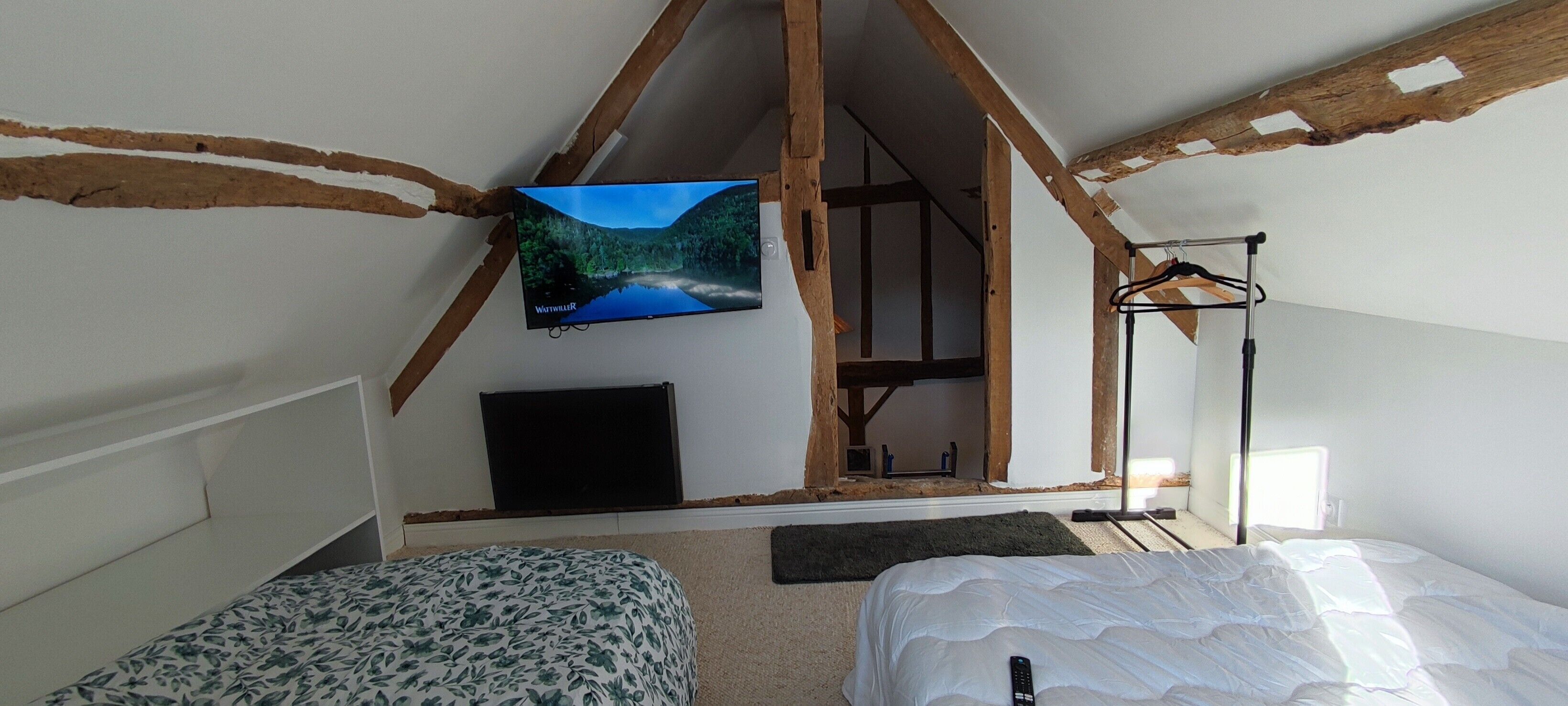 A bedroom with a TV, two beds, a hanging light fixture, and exposed wooden beams.