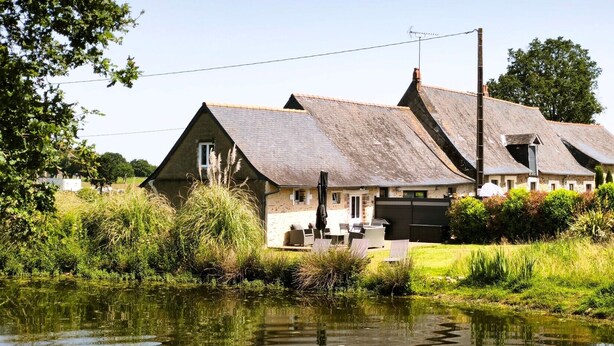 Ein traditionelles Haus mit Teich, umgeben von viel Grün.