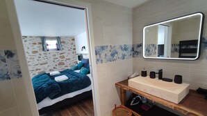 Ein Schlafzimmer mit Bett, Nachttisch aus Holz, einem Spiegel und einem Badezimmer mit Waschbecken und Spiegel.