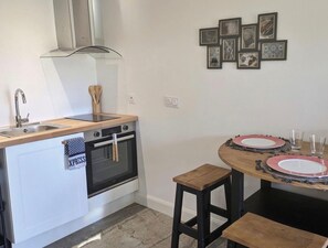 Une cuisine compacte équipée d’une cuisinière, d’un four, d’un évier et d’un petit coin repas avec une table et des tabourets.