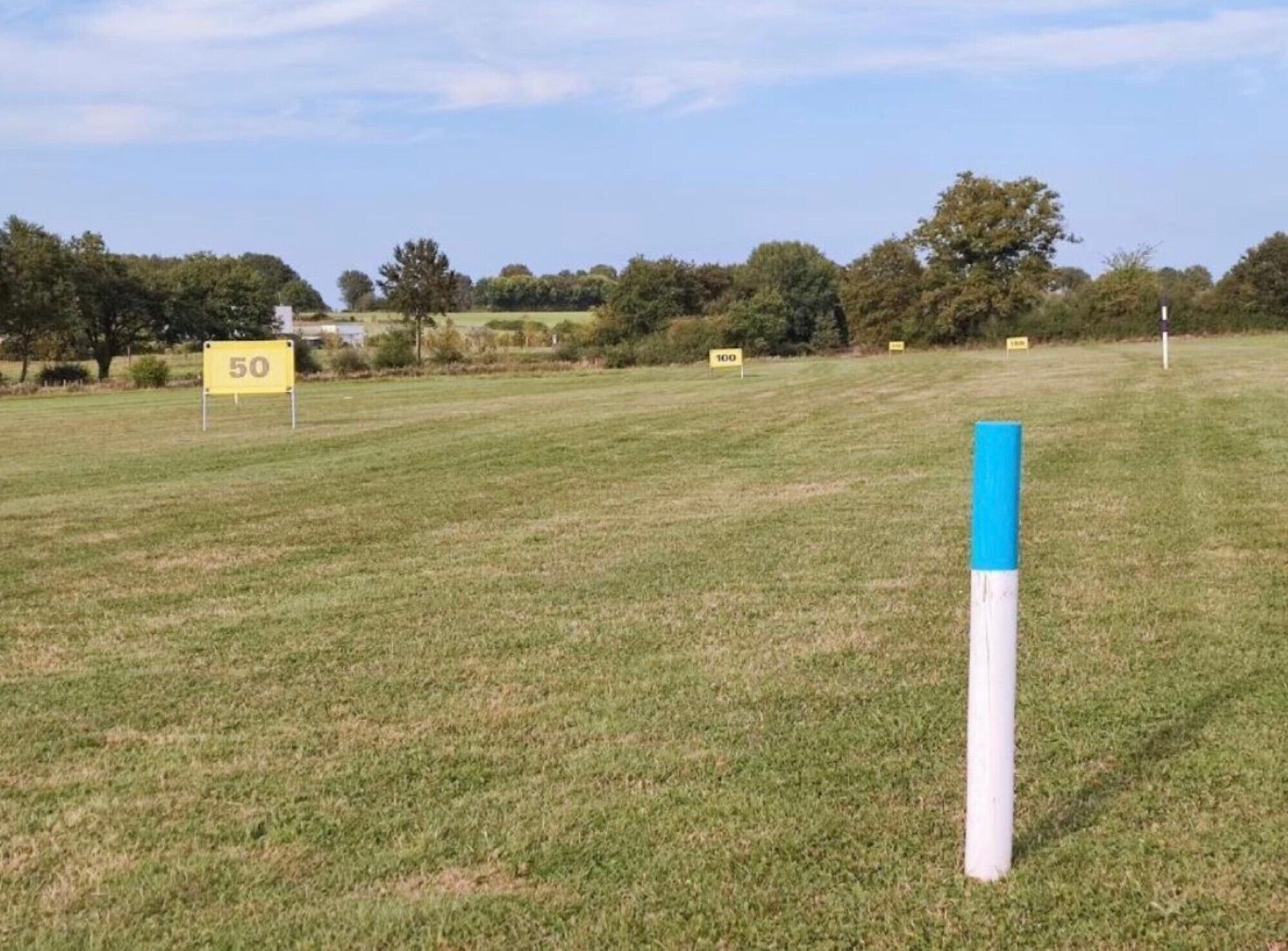 A grassy field with a blue and white post, and yellow signs with numbers.