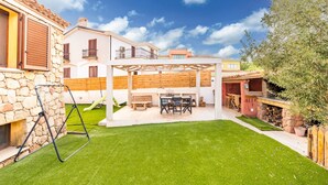Eine Terrasse mit Tisch und Stühlen, eine Steinmauer und eine Pergola.