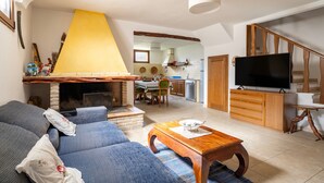 Ein Wohnzimmer mit einer Couch, einem Holztisch, einem Kamin, einem Fernseher und einer Küche im Hintergrund.