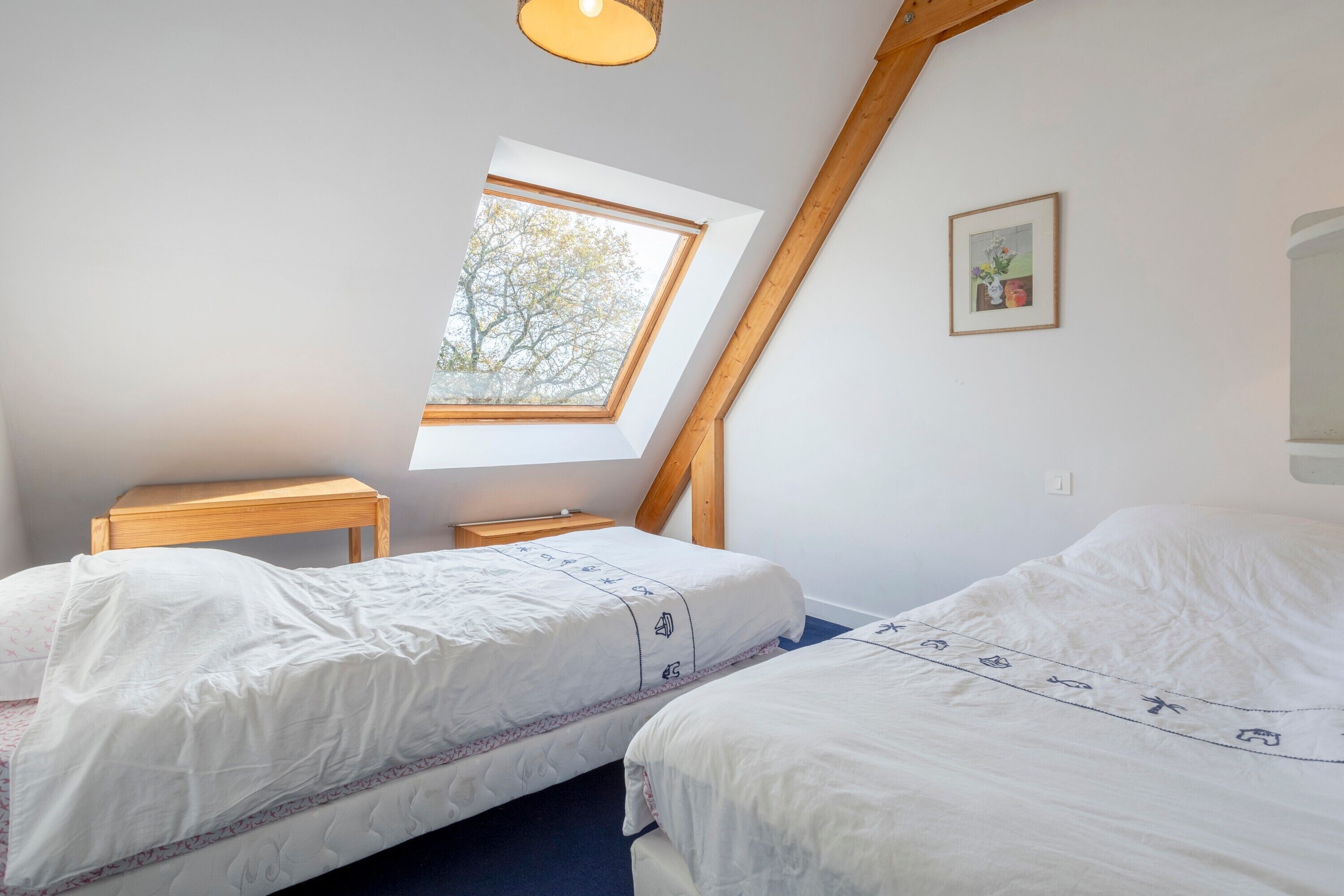 Een slaapkamer met twee bedden, een dakraam, een klein tafeltje en een lijst met een afbeelding aan de muur.