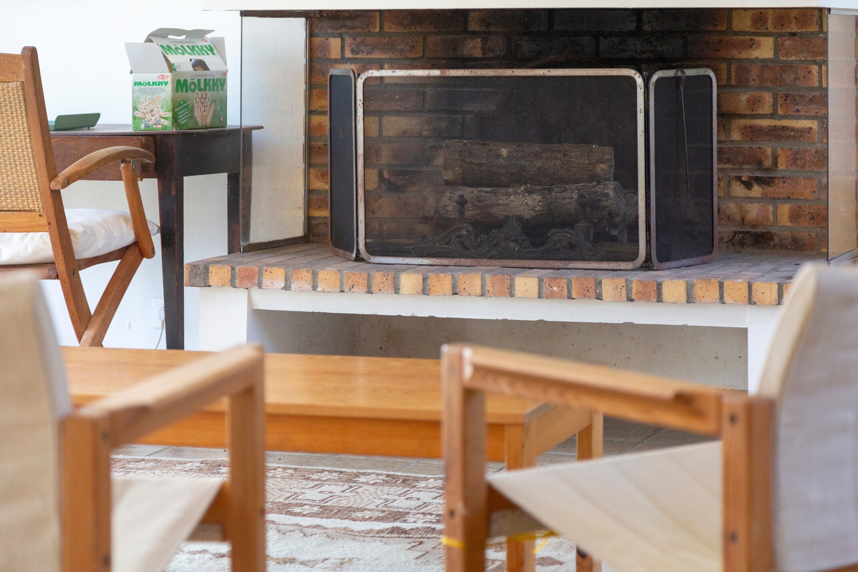A fireplace with a brick surround, a wooden chair, and a table with a box of Molkky cereal.
