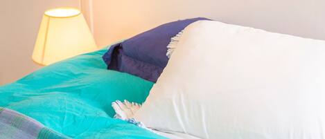 A bed with a teal and white duvet, a dark blue pillow, and a white pillow.