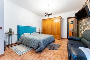 A bedroom with a bed, a wooden wardrobe, a television, and a leather sofa.