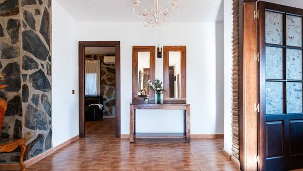 A hallway with a stone wall, a wooden bench, a console table with a vase, and a door with frosted glass panels. - Holiday Home 'The Palm House' with Mountain View, Wi-Fi and Air Conditioning (Las Lagunas de Mijas)