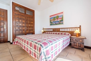 A bedroom with a large bed, a wooden headboard, a nightstand with a lamp, a painting on the wall, and a wooden wardrobe.