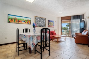 A dining area with a table, chairs, and a vase of flowers. There is a red sofa and a wooden table in the living area.