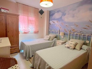 Une chambre avec deux lits, une armoire, une fenêtre avec des rideaux et une fresque murale.