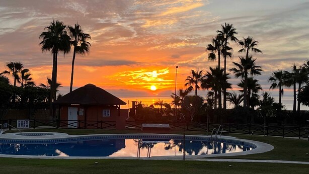 Une piscine dont l’eau reflète les palmiers et le coucher de soleil.