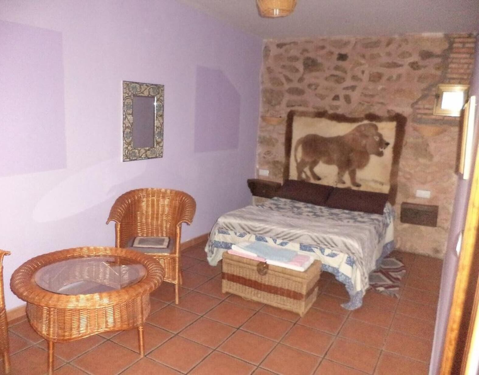 Ein Schlafzimmer mit einem Bett, zwei Korbstühlen, einem kleinen Tisch, einer Steinwand und einem gerahmten Bild.