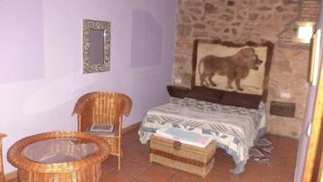 Ein Schlafzimmer mit einem Bett, zwei Korbstühlen, einem kleinen Tisch, einer Steinwand und einem gerahmten Bild.