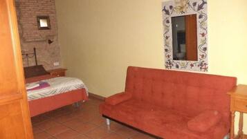 Una stanza con un letto, un divano rosso, un tavolino, uno specchio con cornice decorativa e un muro in mattoni.