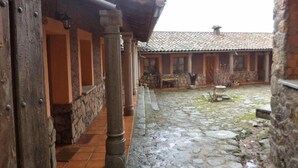 A courtyard with stone flooring, wooden columns, and a building with a tiled roof.