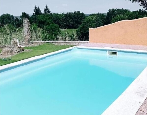A rectangular swimming pool with a clear blue water surface, surrounded by a concrete deck and a grassy area with trees in the background. - Country House 'Mansió De La Plata' with Mountain View, Private Pool and Wi-Fi (PEÑACABALLERA)